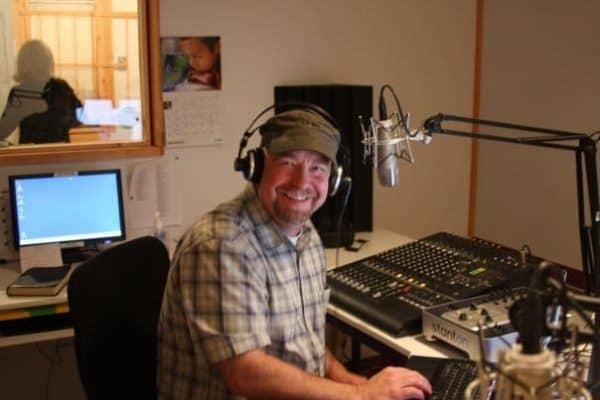 Smiling Radio DJ with headphones on sitting at the broadcast console
